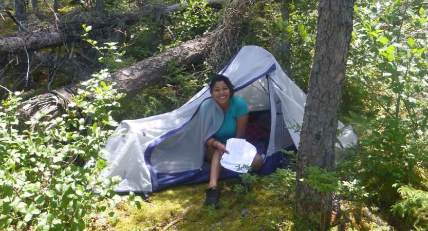 a person smiles from under a tarp shelter amongst trees on an outward bound course
